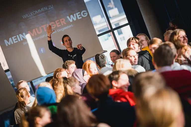 "Ein Bild von einer Menschenmenge bei einer Unterhaltungsveranstaltung, gekleidet in Anzügen, die in Konversation sind und Spaß haben. Das Publikum besteht aus einer Mannschaft, die Leistung zeigt."