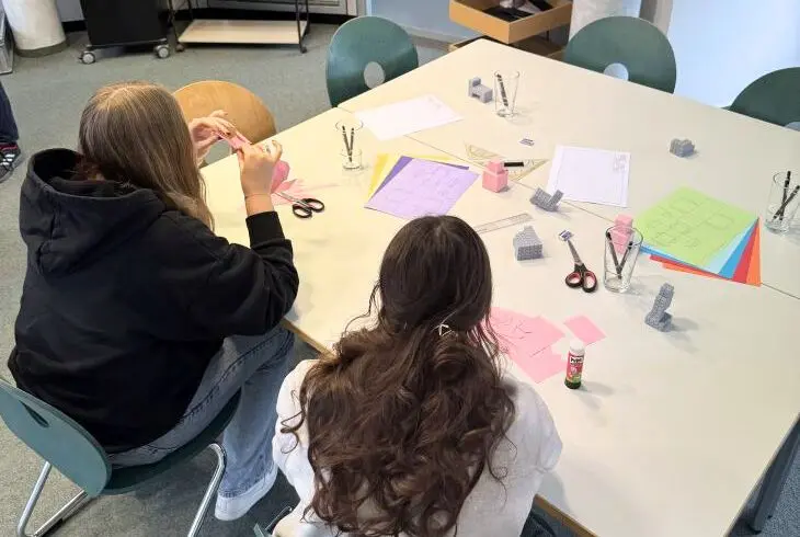 Zwei Jugendliche basteln mit Papiermodellen an einem Tisch
