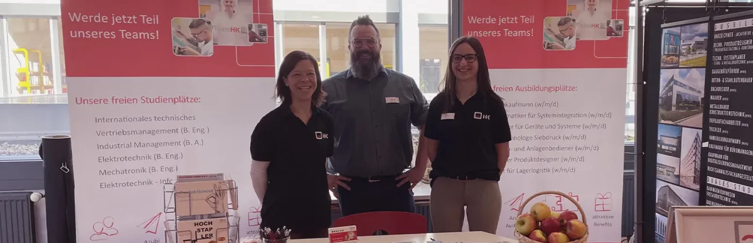 three H+K employees at their own stand at the training fair
